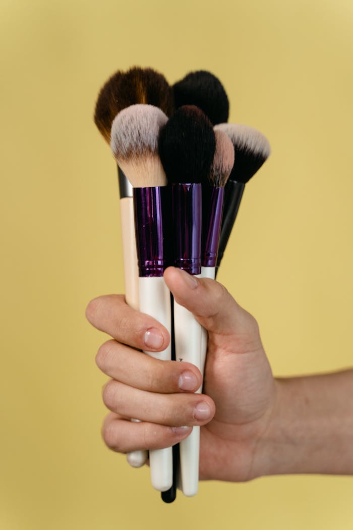About A hand holding various makeup brushes against a yellow background.